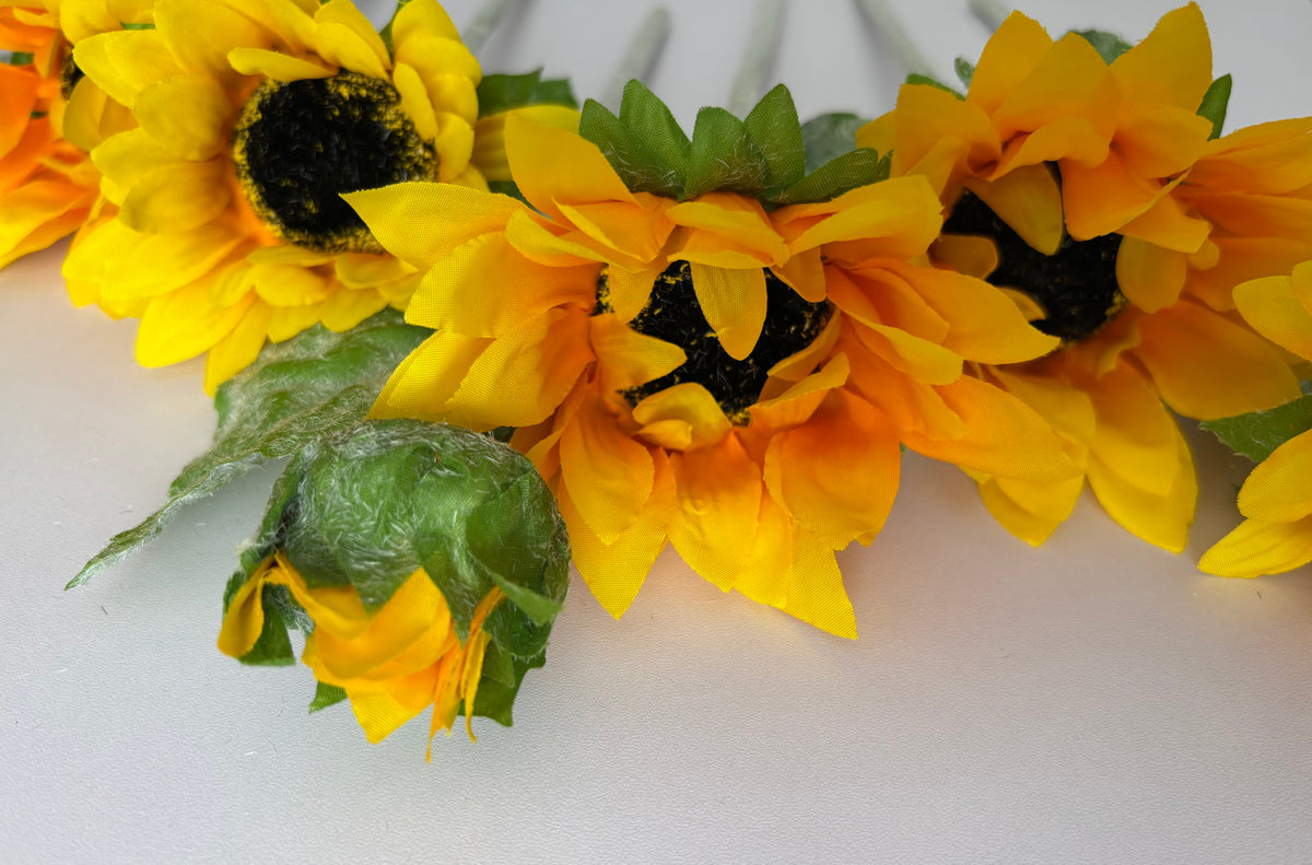 Extreme close up shot of three large artificial sunflower heads showing the stunning golden yellow and deep orange layered petals with dark brown to black textured centres and lush dark green foliage on a plain white background