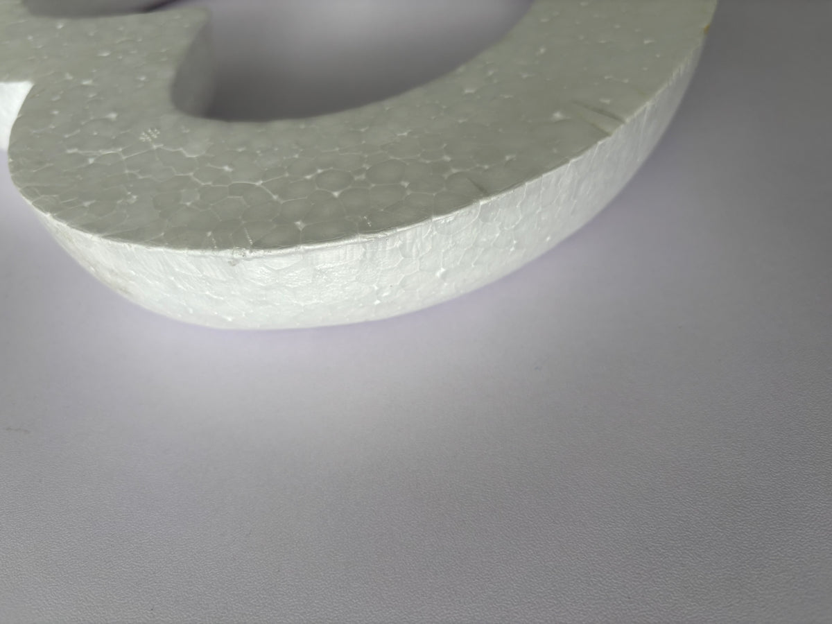 Extreme close up macro shot of the textured porous surface of a white polystyrene heart wreath frame showing the detailed granular polystyrene material texture and curved edge profile clearly against a plain light grey background