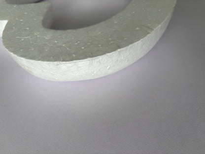Extreme close up macro shot of the textured porous surface of a white polystyrene heart wreath frame showing the detailed granular polystyrene material texture and curved edge profile clearly against a plain light grey background