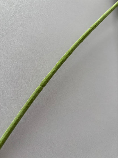 Extreme close up diagonal shot of an artificial purple silk anemone stem showing the soft fabric wrapped wired stem construction in bright green with fine texture detail visible against a plain light grey background