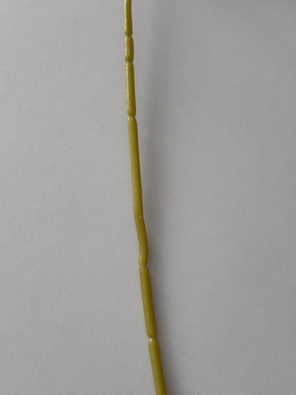 Extreme macro close up vertical shot of the full length yellow-green wired stem of an artificial purple anemone single stem showing the fine textured detail and subtle node joints of the stem on a plain light grey background