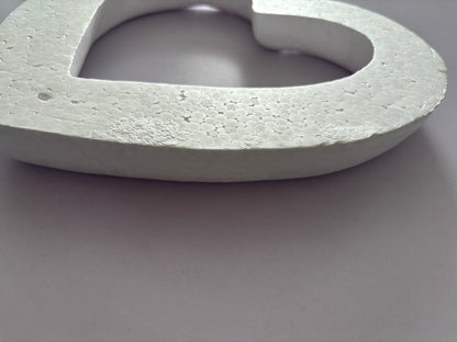Extreme close up macro side profile shot of a white polystyrene heart wreath frame showing the full 3.5cm depth and highly detailed textured granular porous polystyrene cut edge surface with the hollow centre visible against a plain neutral grey background