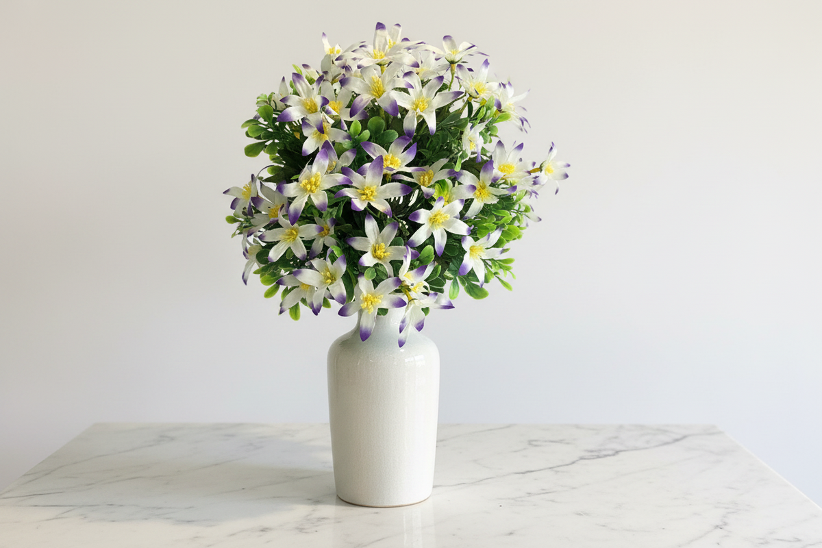  AI generated styling inspiration image showing artificial purple tipped white wild lily bunch arranged in a tall white ceramic vase displayed on a light marble surface against a plain white wall creating an elegant and airy home decor display
