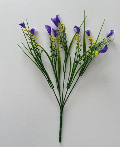 Upright portrait shot of an artificial purple small calla lily foliage bunch showing the full bunch height with five individual wired stems fanning out from a single bottom stem with small purple calla lily flower heads, tall thin green grass stems and small bright yellow berry pick stems against a plain light grey background