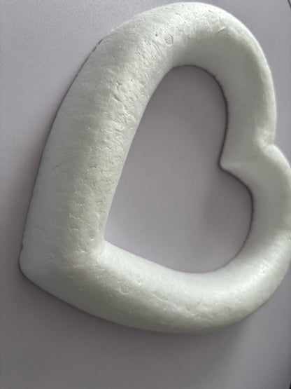 Close up angled overhead shot of a white polystyrene heart wreath frame 28cm showing the thick textured porous polystyrene border and hollow centre cutout in detail against a plain neutral grey background