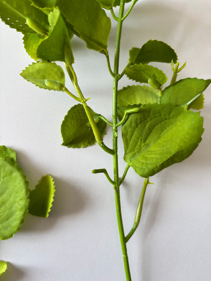 Upright close up shot of an artificial green patchouli leaf foliage spray showing the full stem height with the main wired plastic stem, two branching side stems and multiple rounded serrated green fabric silk patchouli leaves arranged naturally at varying heights against a plain white background
