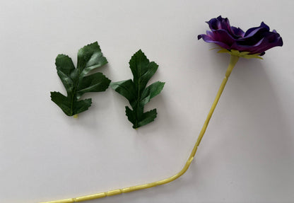 Artificial purple anemone single stem laid flat showing the full length of the yellow-green wired stem with deep purple flower head and two separate dark green serrated foliage leaves displayed individually on a plain white background