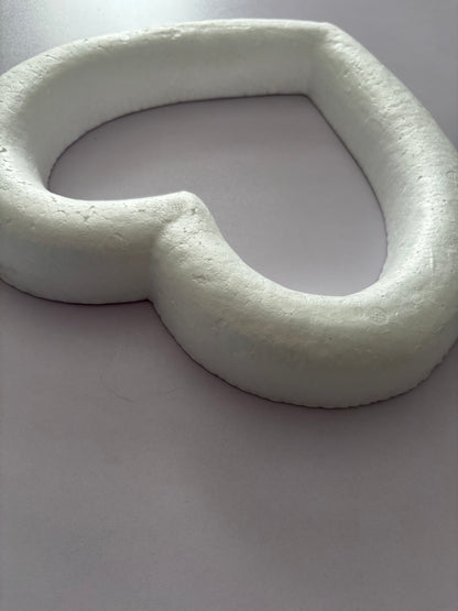 Close up low angle shot of a white polystyrene heart wreath frame 28cm showing the top curved section of the heart shape highlighting the full 3.5cm depth and textured porous polystyrene surface construction against a plain light grey background