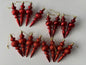 Flat lay of all 16 red Christmas spindle baubles in matte, metallic and glittered finishes with ribbed spherical tops, beaded middles and elongated pointed drop bases with gold hanging strings arranged in two rows on a plain white background