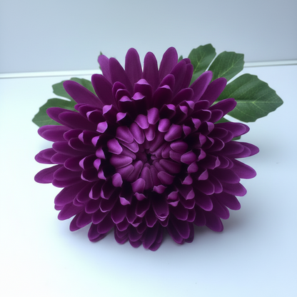 Close up of a single artificial deep purple chrysanthemum flower head with tightly packed layered petals and green leaves visible at the base on a plain light grey background