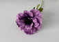 Overhead angled shot of an artificial purple silk anemone flower head showing beautifully open layered cup-shaped petals with fine vein detail throughout, a dramatic dark black raised centre and bright green detachable serrated foliage leaves visible behind against a plain light grey background