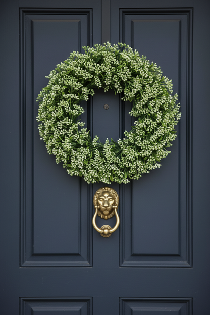 Artificial green berry stems styled in a round door wreath with lush green foliage on a dark navy front door with gold lion door knocker