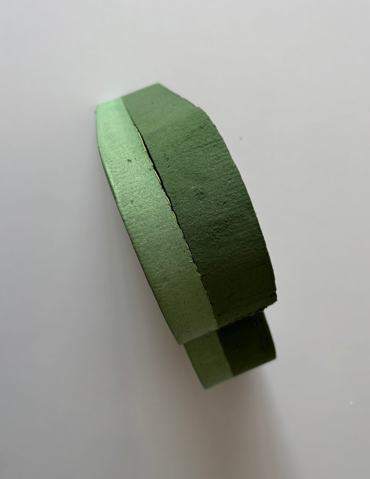 Upright standing shot of a green heart shaped oasis wet floral foam frame balanced on its base edge showing the full 6cm depth and thick two layer foam construction from the side clearly against a plain off white background