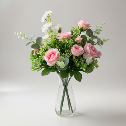 Artificial green berry stems styled in a mixed floral arrangement with pink roses, white blossoms and eucalyptus leaves in a clear glass vase on grey background