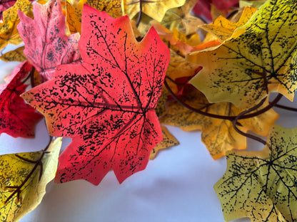 Extreme close up macro shot of multiple silk maple leaves from an autumn maple leaf garland showing rich red, pink, orange, yellow and green colour tones with detailed black leaf vein markings and realistic leaf texture against a plain white background