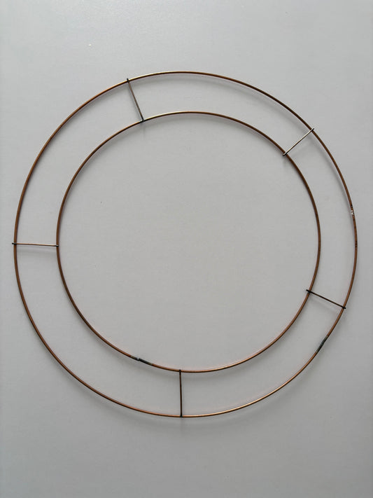 Overhead flat lay shot of a copper-toned double ring wire wreath frame 35cm showing the two concentric circular rings and vertical support wires against a plain light grey background