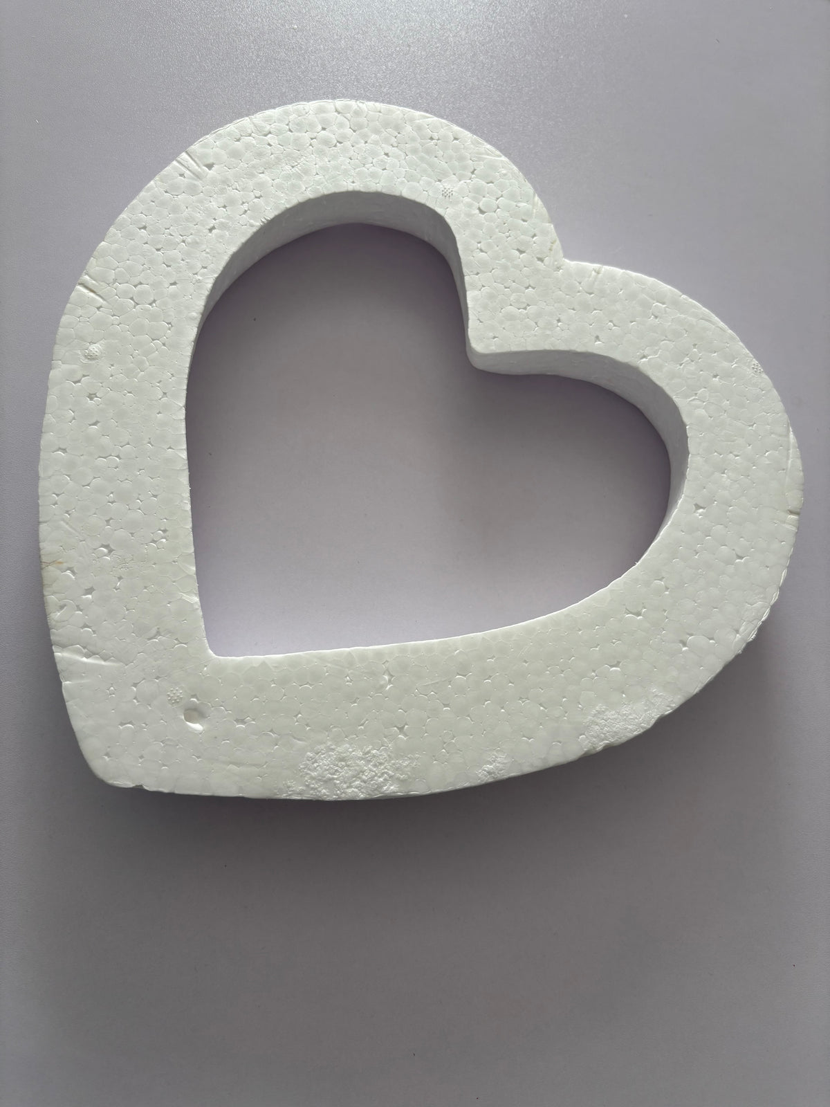 Front facing flat lay shot of a white polystyrene heart wreath frame 28cm showing the full hollow heart shape with thick solid polystyrene border and smooth flat front face clearly against a plain neutral grey background