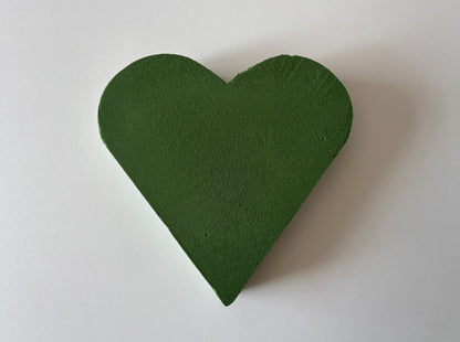Close up overhead flat lay shot of a green heart shaped oasis wet floral foam frame showing the detailed porous textured foam surface clearly against a plain white background highlighting the soft wet foam top layer ideal for fresh flower and artificial stem insertion