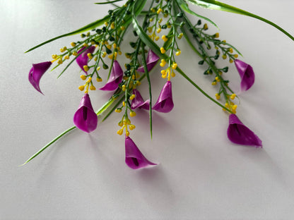 Overhead flat lay shot of an artificial pink small calla lily foliage bunch held from above showing all five stems drooping naturally downward with small bright magenta pink calla lily flower heads hanging down and bright yellow berry pick stems and thin green grass stems cascading against a plain light grey background