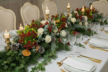 Artificial red berry and foliage stems styled in an elegant Christmas wedding table runner with white roses, red berries, pine cones and candles on a white linen banquet table