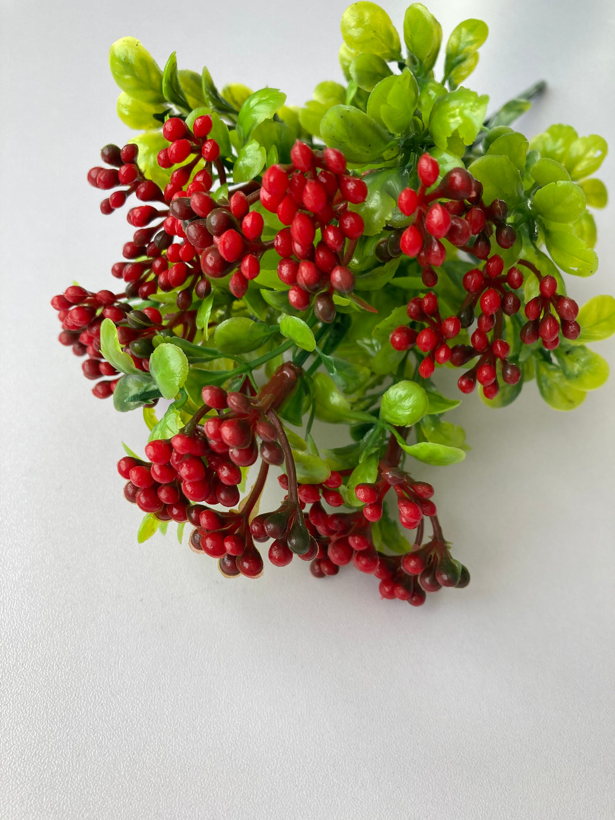 Top down view of artificial red berry and foliage bunch showing dense red berry clusters amongst bright green leaves on white background